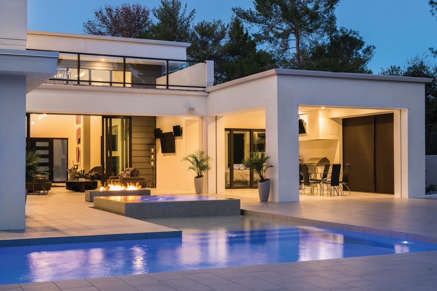 Modern home with lit patio, fire feature and pool at dusk